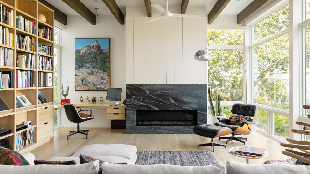This is an example of a living room in Portland Maine with white walls, light hardwood floors, a ribbon fireplace, a stone fireplace surround, beige floor and exposed beam.