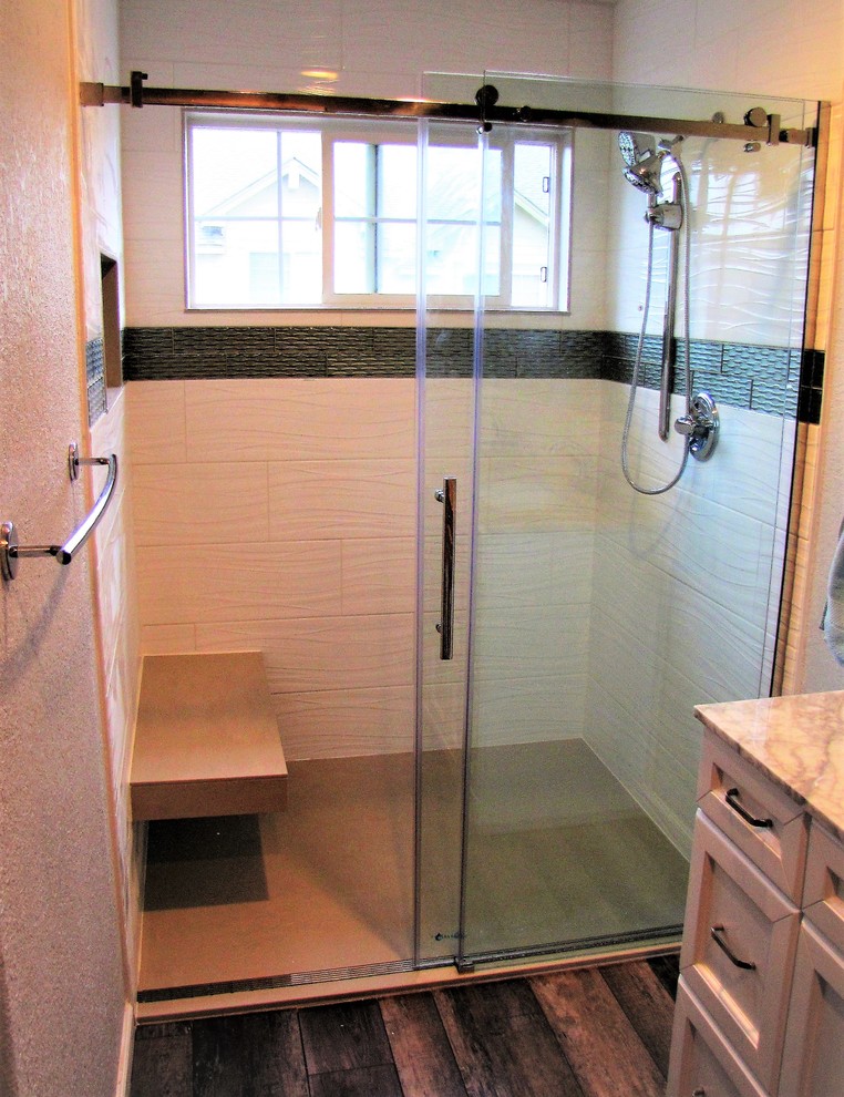Photo of a mid-sized arts and crafts master bathroom in Denver with raised-panel cabinets, white cabinets, a curbless shower, gray tile, porcelain tile, vinyl floors, marble benchtops, brown floor, a sliding shower screen and white benchtops.