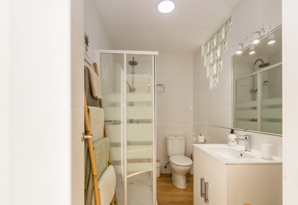Idéer för ett litet minimalistiskt badrum med dusch, med en hörndusch, en toalettstol med hel cisternkåpa, vit kakel, vita väggar, ljust trägolv, ett undermonterad handfat och dusch med skjutdörr