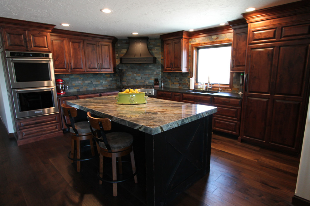 Inspiration for a large rustic medium tone wood floor and brown floor kitchen remodel with an undermount sink, raised-panel cabinets, medium tone wood cabinets, granite countertops, multicolored backsplash, stone tile backsplash, paneled appliances, an island and multicolored countertops