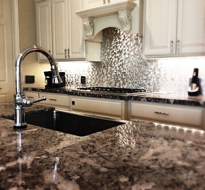 Inspiration for a mid-sized transitional l-shaped travertine floor eat-in kitchen remodel in Houston with a farmhouse sink, raised-panel cabinets, white cabinets, granite countertops, metallic backsplash, metal backsplash, stainless steel appliances and an island