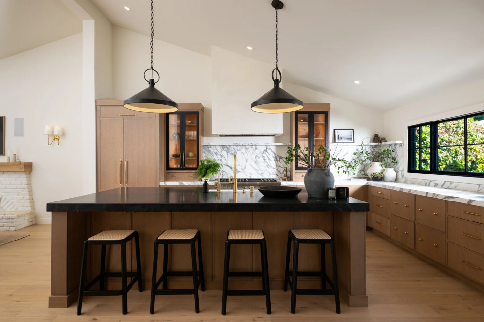 Inspiration for a transitional u-shaped light wood floor, brown floor and vaulted ceiling open concept kitchen remodel in Orange County with a farmhouse sink, flat-panel cabinets, light wood cabinets, marble countertops, multicolored backsplash, marble backsplash, stainless steel appliances, an island and multicolored countertops