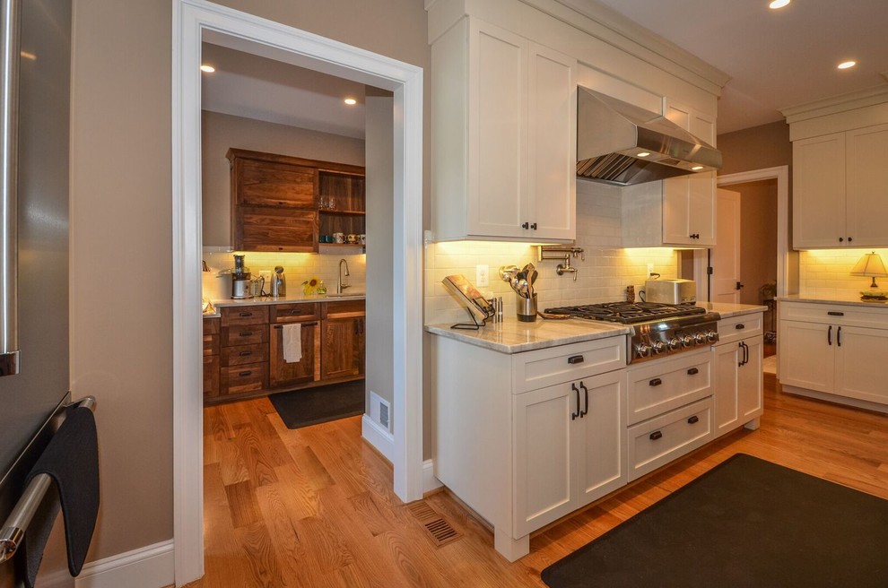 This is an example of a large country eat-in kitchen in DC Metro with a drop-in sink, shaker cabinets, dark wood cabinets, quartzite benchtops, white splashback, porcelain splashback, stainless steel appliances, light hardwood floors, with island and brown floor.