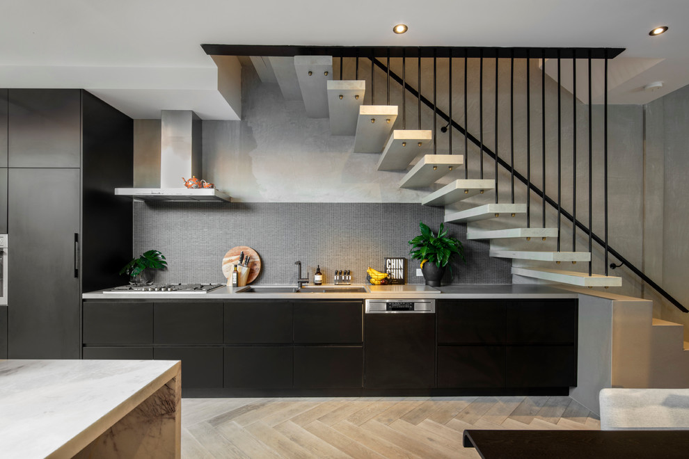 This is an example of a mid-sized contemporary single-wall open plan kitchen in Melbourne with an undermount sink, black cabinets, marble benchtops, black splashback, mosaic tile splashback, stainless steel appliances, light hardwood floors and with island.