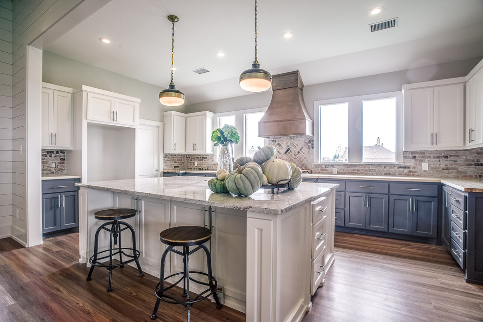 Mid-sized country u-shaped open plan kitchen in Austin with recessed-panel cabinets, white cabinets, marble benchtops, multi-coloured splashback, brick splashback, medium hardwood floors, with island, beige floor, stainless steel appliances and an undermount sink.