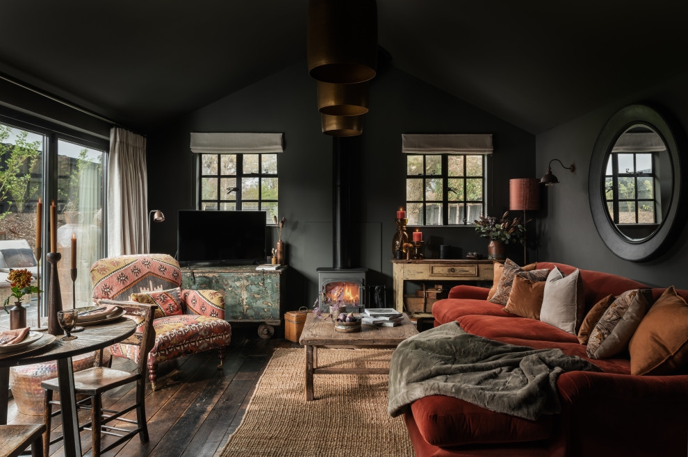 Cette image montre un salon rustique de taille moyenne et ouvert avec un mur gris, parquet foncé, un poêle à bois, un manteau de cheminée en plâtre, un téléviseur indépendant, un plafond voûté et éclairage.