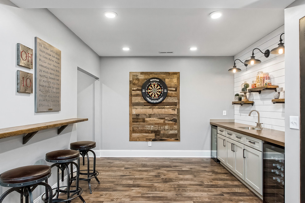 Mid-sized country single-wall seated home bar in Columbus with a drop-in sink, shaker cabinets, white cabinets, wood benchtops, white splashback, timber splashback, medium hardwood floors, brown floor and brown benchtop.