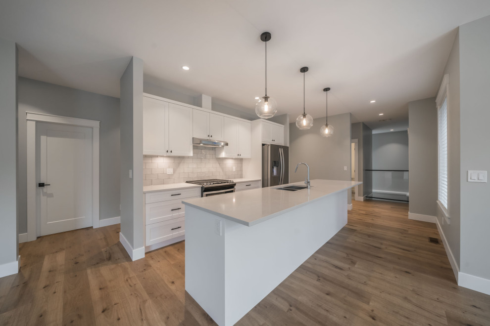 Mid-sized modern single-wall open plan kitchen in Other with a double-bowl sink, white cabinets, white splashback, subway tile splashback, stainless steel appliances, medium hardwood floors, with island, brown floor and white benchtop.