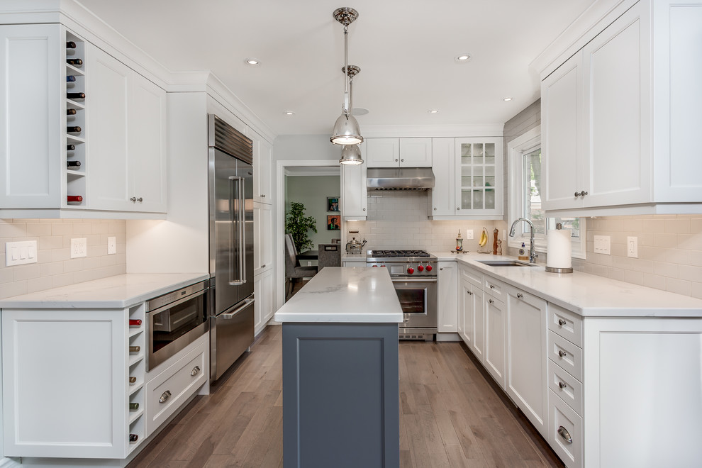Large transitional galley eat-in kitchen in Toronto with an undermount sink, shaker cabinets, white cabinets, quartzite benchtops, white splashback, subway tile splashback, stainless steel appliances, dark hardwood floors, with island and brown floor.