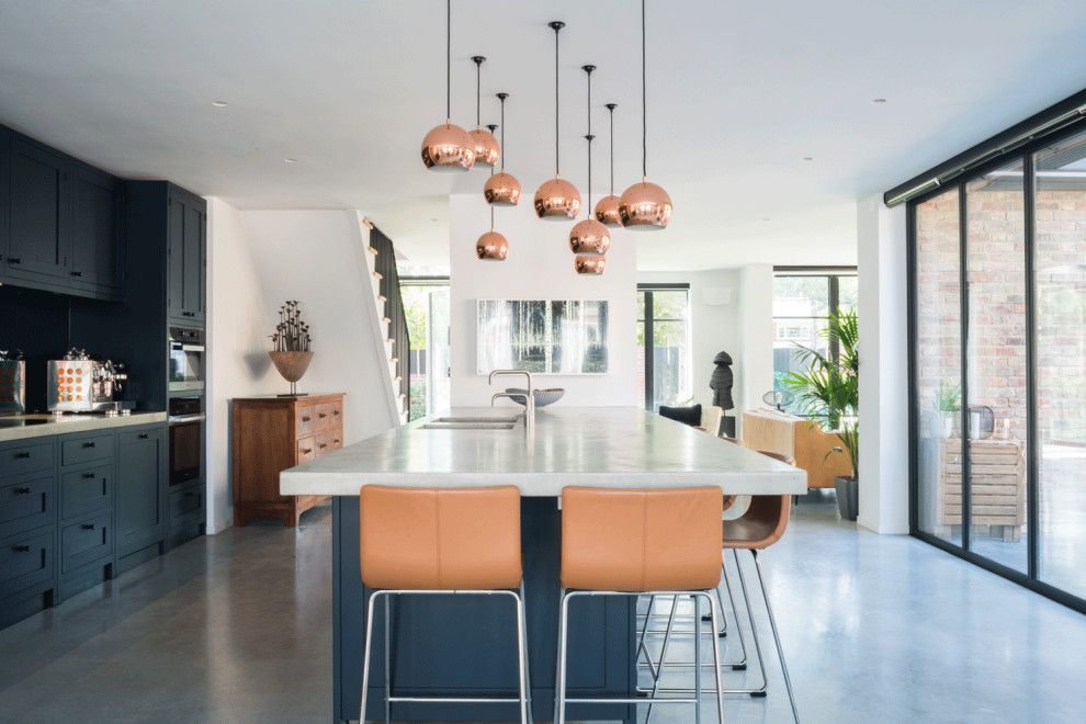 Large contemporary open plan kitchen in London with a submerged sink, recessed-panel cabinets, blue cabinets, concrete worktops, blue splashback, stainless steel appliances, concrete flooring, an island, grey floors and white worktops.