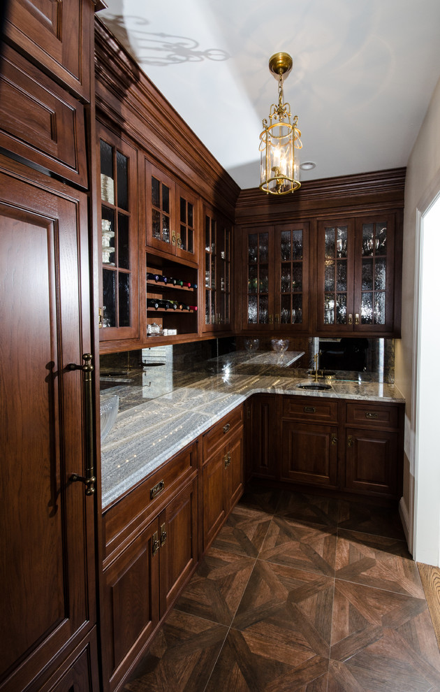 Photo of a small traditional single-wall wet bar in New York with an undermount sink, raised-panel cabinets, dark wood cabinets, granite benchtops, mirror splashback, dark hardwood floors and brown floor.