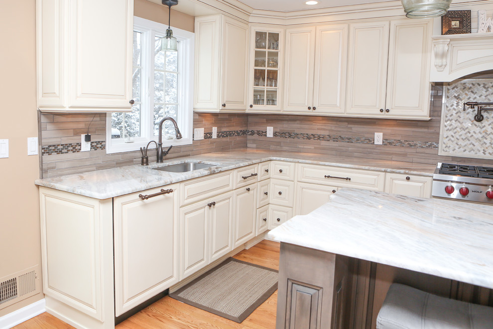 Large transitional u-shaped light wood floor eat-in kitchen photo in Newark with an undermount sink, raised-panel cabinets, distressed cabinets, granite countertops, brown backsplash, mosaic tile backsplash, stainless steel appliances and an island