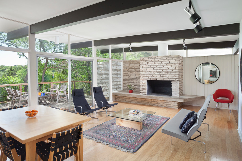 This is an example of a midcentury open concept living room in Austin with light hardwood floors, a standard fireplace and a stone fireplace surround.