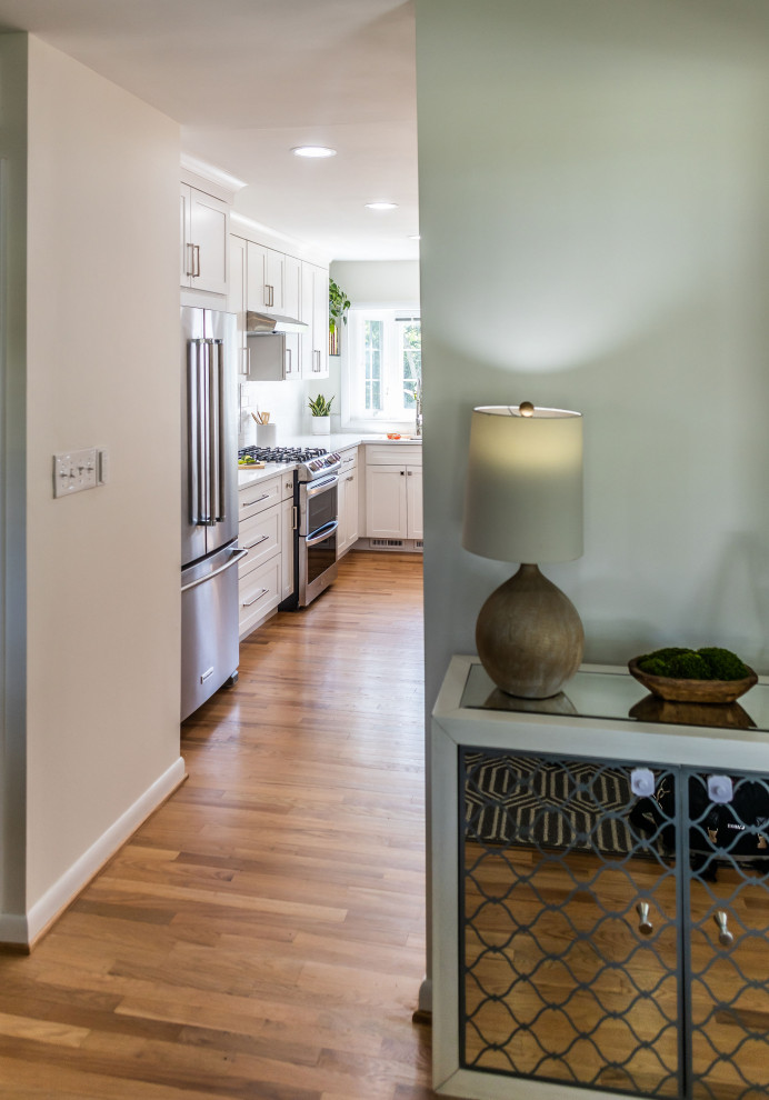 Mid-sized transitional l-shaped light wood floor and brown floor eat-in kitchen photo in Baltimore with an undermount sink, shaker cabinets, white cabinets, quartz countertops, white backsplash, marble backsplash, stainless steel appliances, an island and white countertops