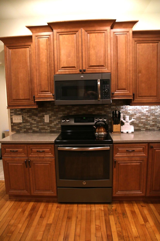 Example of a mid-sized transitional l-shaped medium tone wood floor enclosed kitchen design with an undermount sink, raised-panel cabinets, medium tone wood cabinets, granite countertops, beige backsplash, mosaic tile backsplash, stainless steel appliances and an island