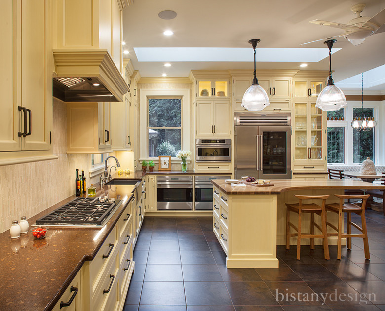 Photo of a large traditional l-shaped eat-in kitchen in Charlotte with beige splashback, stainless steel appliances, ceramic floors, with island, a farmhouse sink, beaded inset cabinets, yellow cabinets, quartz benchtops and ceramic splashback.