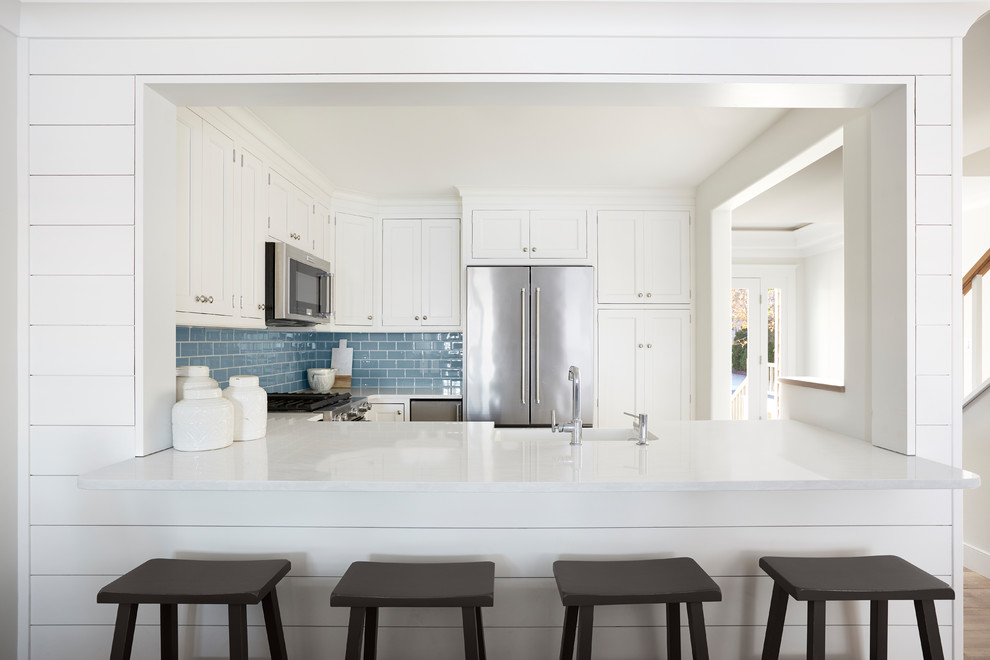 Inspiration for a mid-sized beach style u-shaped separate kitchen in Other with shaker cabinets, white cabinets, blue splashback, subway tile splashback, medium hardwood floors, a peninsula, brown floor, white benchtop, a farmhouse sink, quartz benchtops and stainless steel appliances.