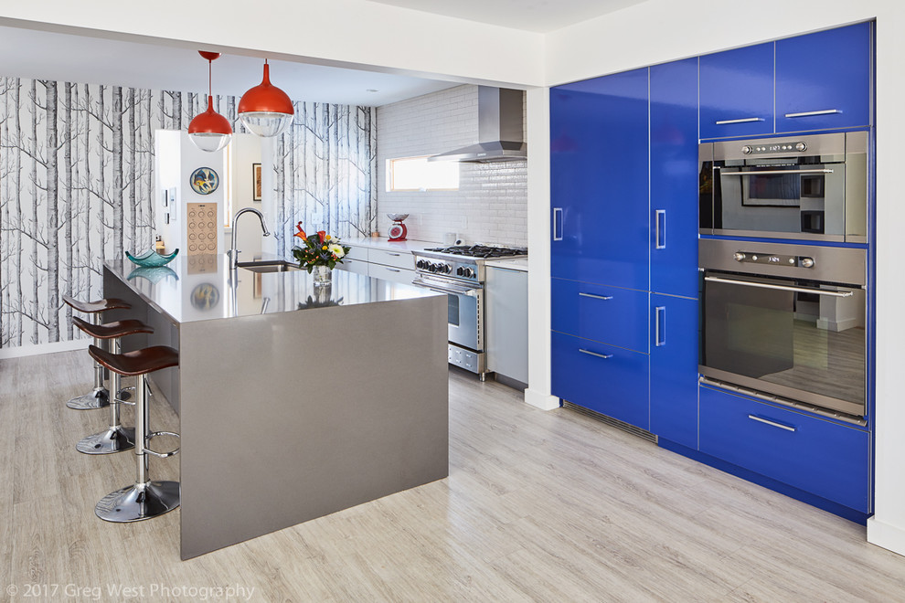 Mid-sized contemporary galley open plan kitchen in Boston with an undermount sink, flat-panel cabinets, stainless steel cabinets, quartz benchtops, white splashback, ceramic splashback, stainless steel appliances, vinyl floors and with island.