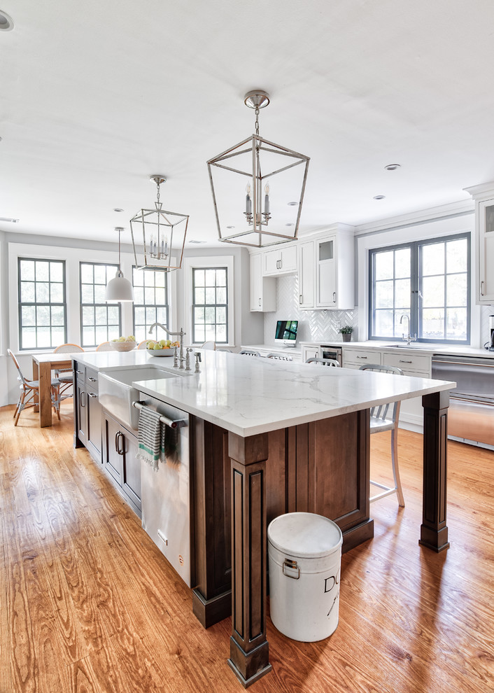 Photo of an expansive traditional galley eat-in kitchen in New York with a farmhouse sink, beaded inset cabinets, white cabinets, quartzite benchtops, white splashback, subway tile splashback, stainless steel appliances, medium hardwood floors, with island and white benchtop.