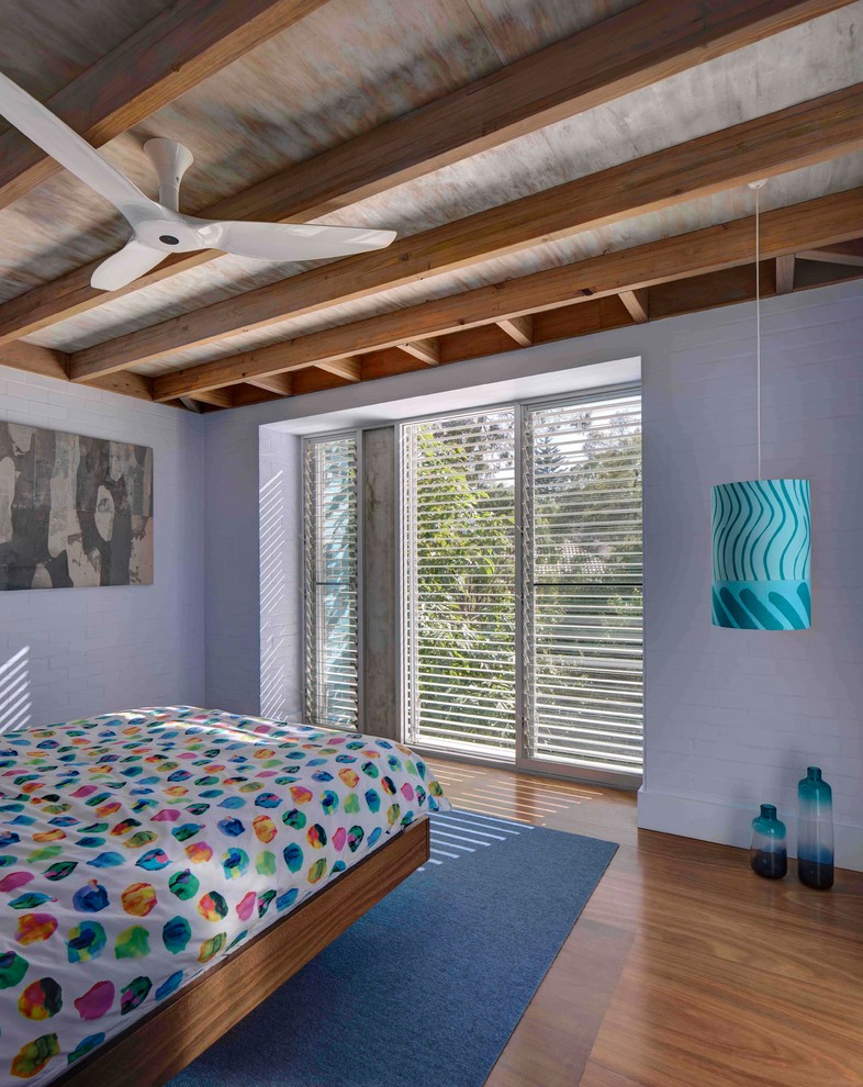 Photo of a tropical bedroom in Sydney with purple walls, medium hardwood floors and brown floor.