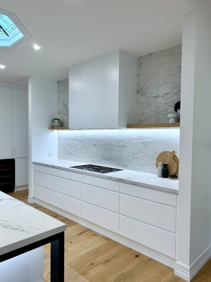 Example of a large l-shaped light wood floor and brown floor open concept kitchen design in Newcastle - Maitland with an undermount sink, flat-panel cabinets, white cabinets, quartz countertops, gray backsplash, quartz backsplash, black appliances, an island and gray countertops