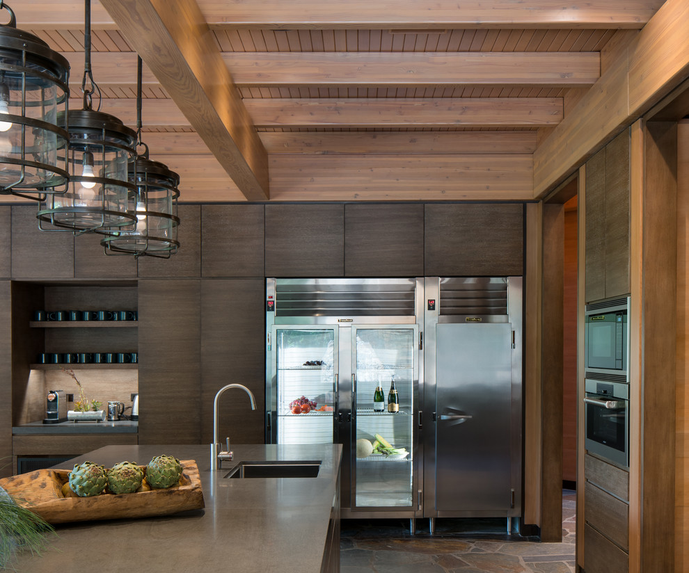 This is an example of an industrial eat-in kitchen in Other with a farmhouse sink, flat-panel cabinets, dark wood cabinets, limestone benchtops, grey splashback, stainless steel appliances and with island.