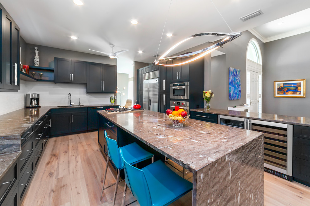 This is an example of a contemporary kitchen in Tampa with an undermount sink, shaker cabinets, black cabinets, quartzite benchtops, white splashback, brick splashback, stainless steel appliances, light hardwood floors and with island.