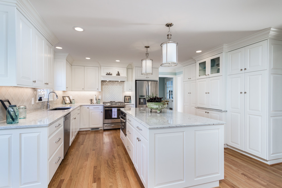 This is an example of a mid-sized traditional u-shaped open plan kitchen in Raleigh with an undermount sink, raised-panel cabinets, white cabinets, granite benchtops, stainless steel appliances, medium hardwood floors, with island, beige splashback, porcelain splashback and beige floor.