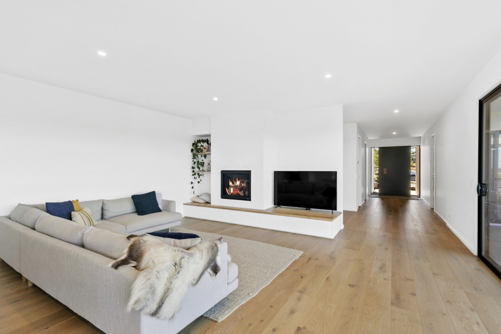 This is an example of a mid-sized contemporary open concept living room in Geelong with white walls, light hardwood floors, a standard fireplace, a plaster fireplace surround and a freestanding tv.