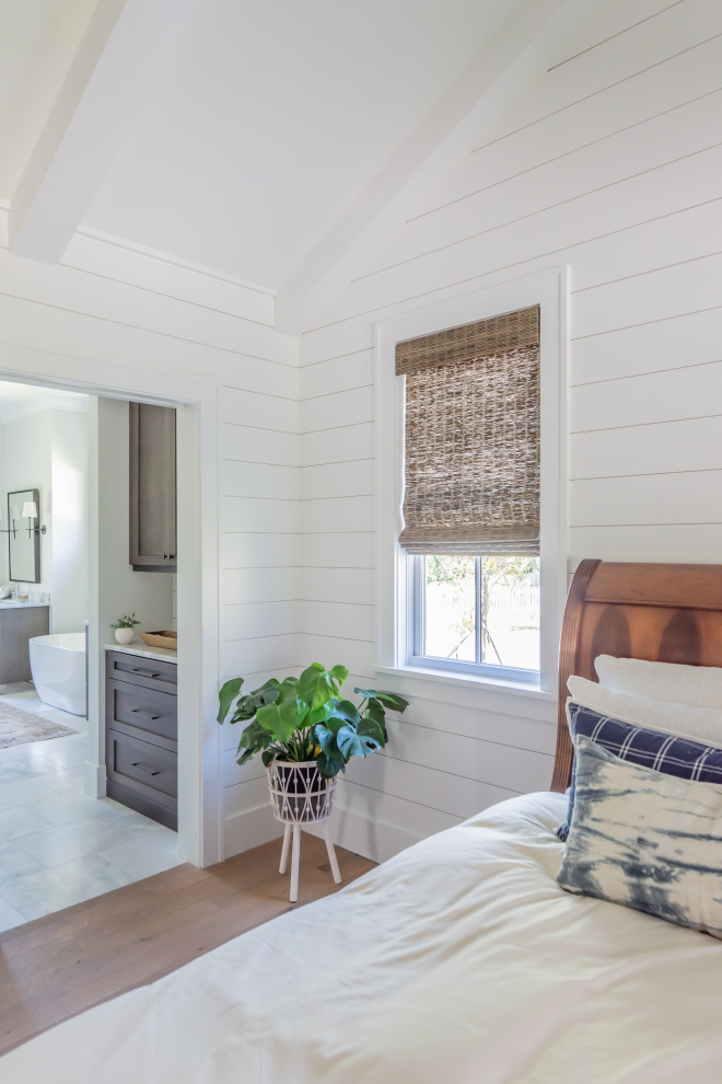 This is an example of a beach style master bedroom with white walls, light hardwood floors, vaulted and planked wall panelling.