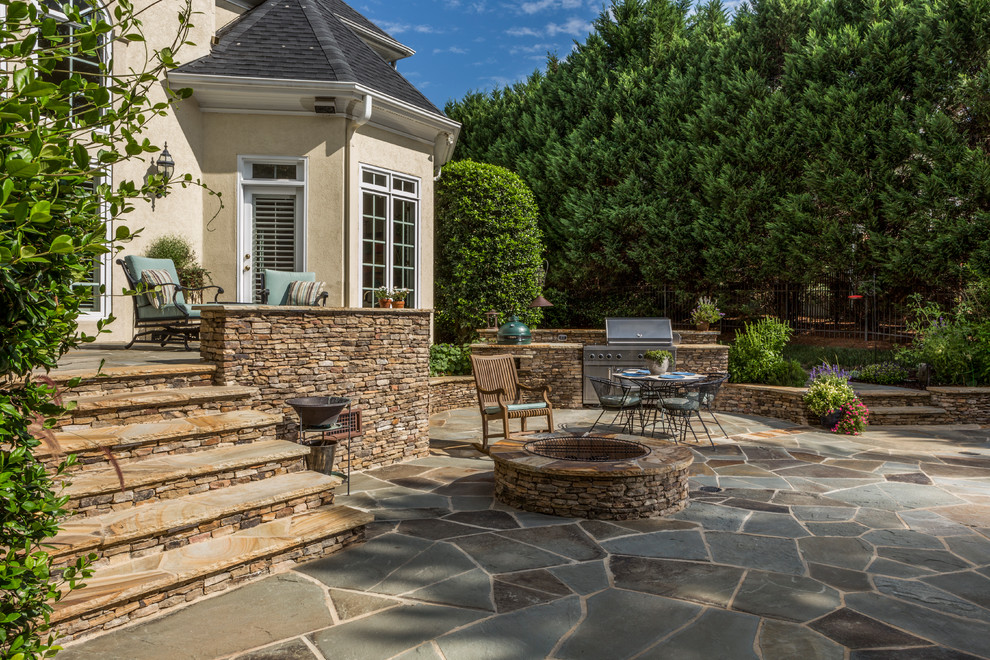 This is an example of a mid-sized traditional backyard patio in Charlotte with a fire feature, natural stone pavers and no cover.