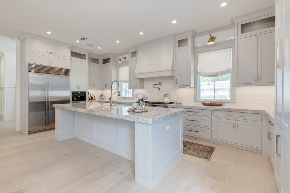 Country u-shaped eat-in kitchen in Dallas with a farmhouse sink, shaker cabinets, grey cabinets, quartzite benchtops, white splashback, ceramic splashback, stainless steel appliances, light hardwood floors, with island, beige floor and beige benchtop.