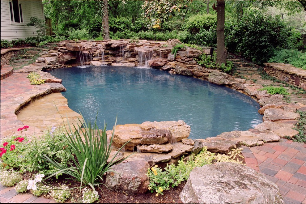 Photo of a mid-sized eclectic backyard custom-shaped natural pool in Houston with a water feature and natural stone pavers.