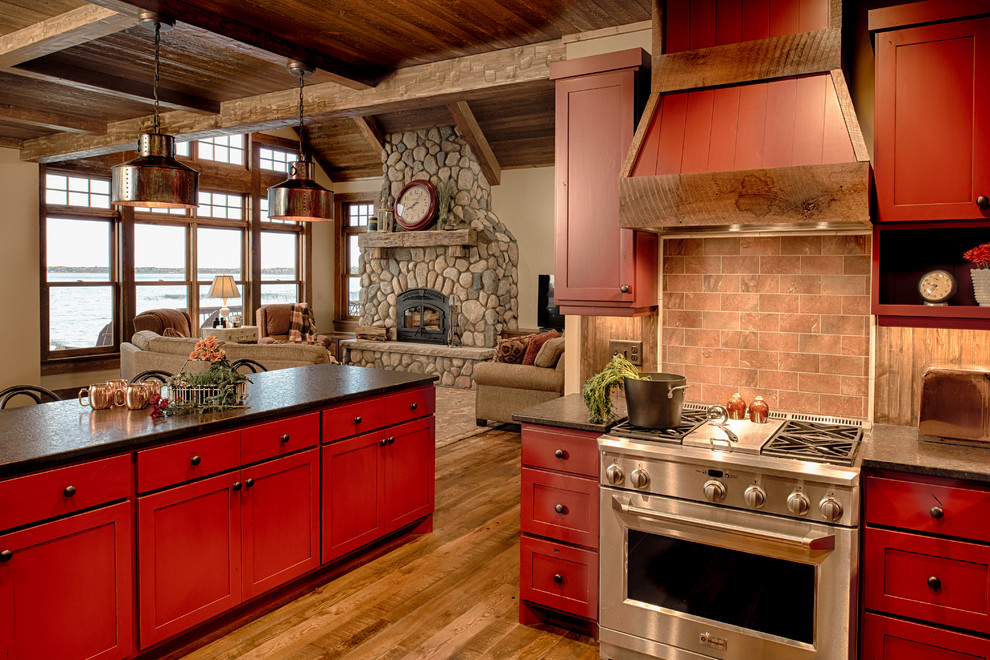 Inspiration for a mid-sized country u-shaped eat-in kitchen in Minneapolis with raised-panel cabinets, red cabinets, solid surface benchtops, red splashback, terra-cotta splashback, stainless steel appliances, with island and medium hardwood floors.