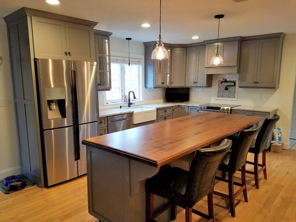 Eat-in kitchen - mid-sized transitional galley light wood floor and brown floor eat-in kitchen idea with a farmhouse sink, recessed-panel cabinets, gray cabinets, wood countertops, white backsplash, subway tile backsplash, stainless steel appliances and an island