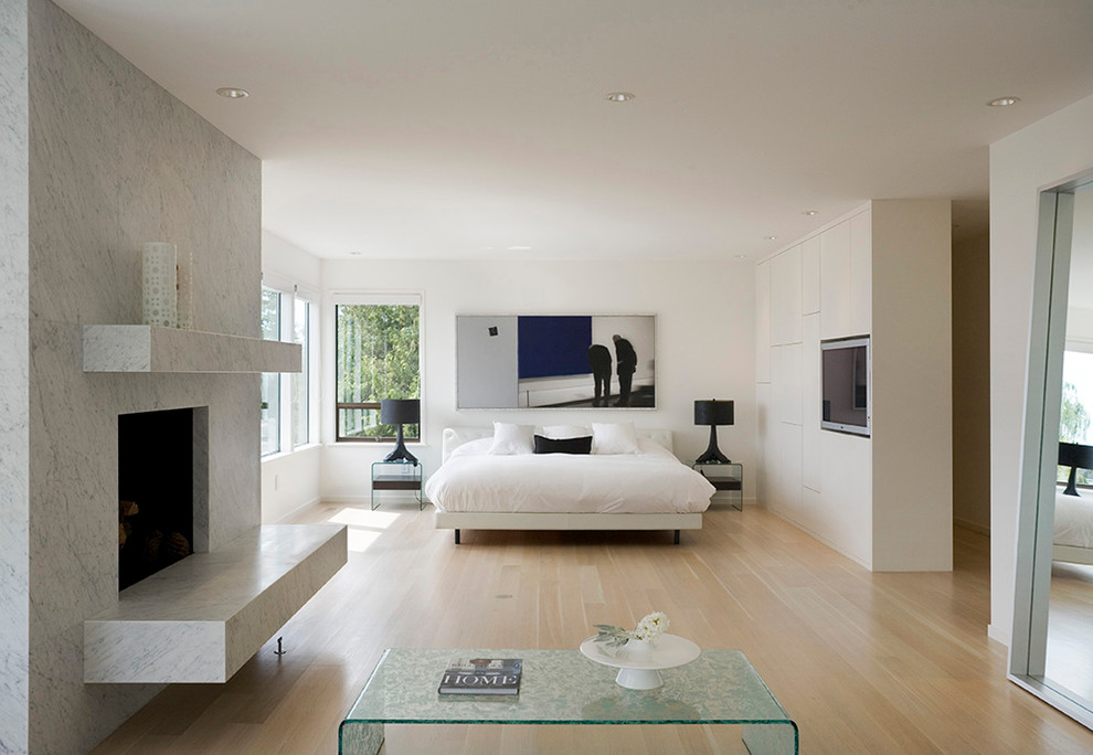 This is an example of a contemporary master bedroom in Seattle with white walls, light hardwood floors and a standard fireplace.