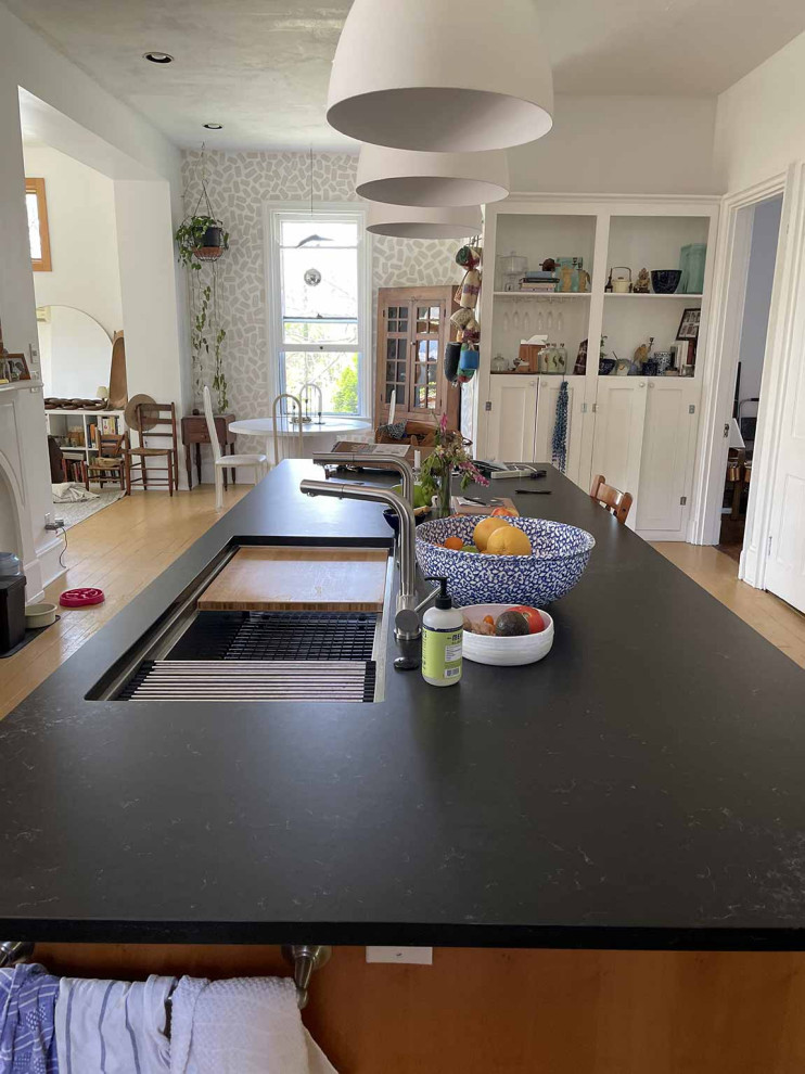This is an example of a large eclectic l-shaped eat-in kitchen in Cincinnati with a single-bowl sink, shaker cabinets, brown cabinets, quartz benchtops, green splashback, ceramic splashback, stainless steel appliances, with island, yellow floor, black benchtop and painted wood floors.