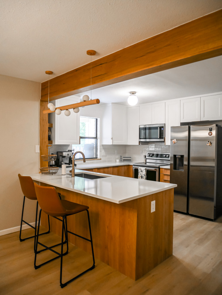 This is an example of a small scandinavian u-shaped eat-in kitchen in Austin with an undermount sink, medium wood cabinets, quartz benchtops, white splashback, porcelain splashback, stainless steel appliances, vinyl floors, a peninsula, brown floor and white benchtop.