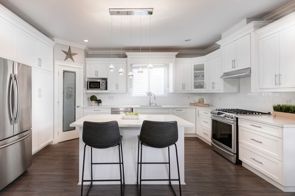 Example of a transitional u-shaped dark wood floor and brown floor kitchen design in Vancouver with an undermount sink, recessed-panel cabinets, white cabinets, white backsplash, stainless steel appliances, an island and gray countertops