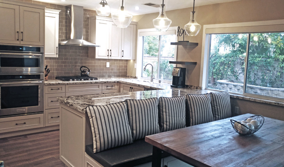 This is an example of a mid-sized country u-shaped kitchen in San Diego with a single-bowl sink, beige cabinets, granite benchtops, grey splashback, glass tile splashback, stainless steel appliances, porcelain floors, a peninsula, brown floor and multi-coloured benchtop.