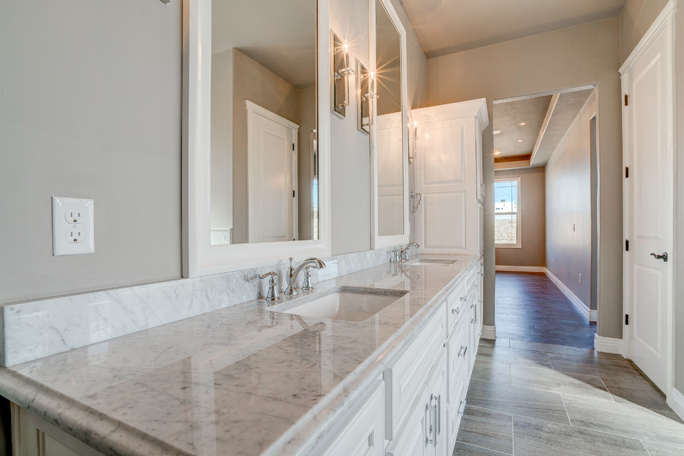 This is an example of a large traditional master bathroom in Austin with raised-panel cabinets, white cabinets, a freestanding tub, an alcove shower, a two-piece toilet, grey walls, ceramic floors, an undermount sink and marble benchtops.