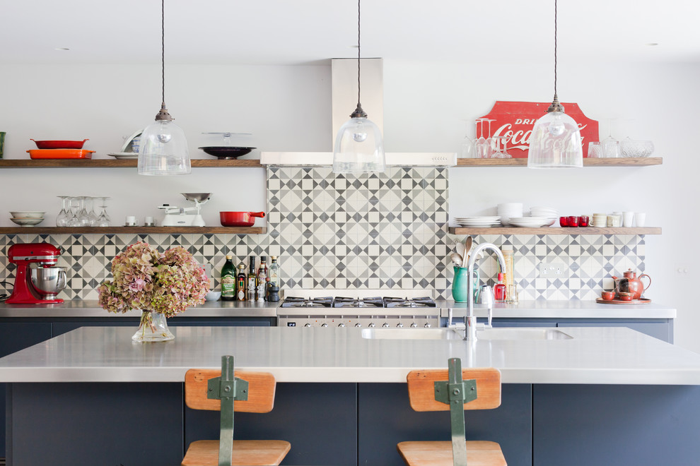 This is an example of a mid-sized contemporary kitchen in London with an integrated sink, stainless steel benchtops, cement tile splashback, stainless steel appliances, open cabinets, multi-coloured splashback and with island.
