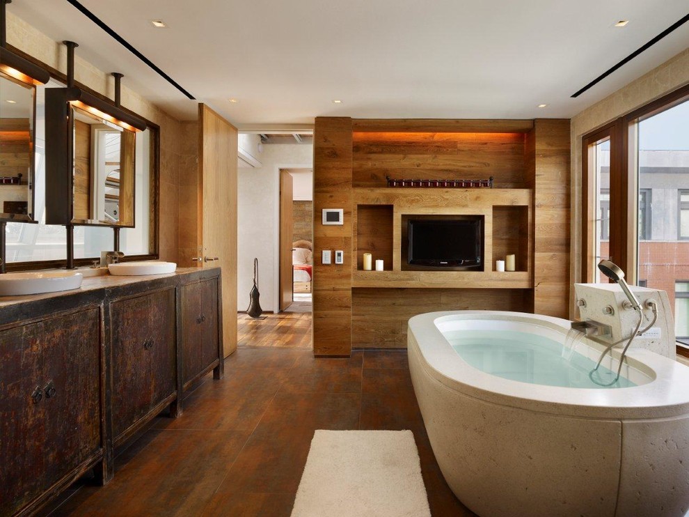 This is an example of a large industrial master bathroom in New York with a vessel sink, flat-panel cabinets, dark wood cabinets, a freestanding tub, beige walls, medium hardwood floors and brown floor.