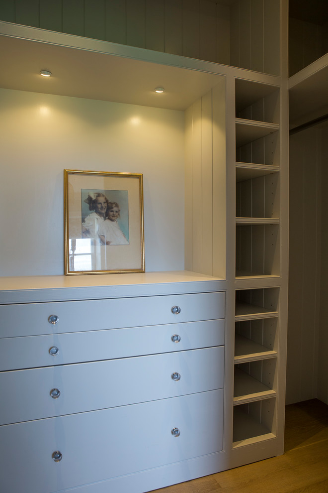 Photo of a mid-sized traditional gender-neutral dressing room in Oxfordshire with flat-panel cabinets, white cabinets and light hardwood floors.
