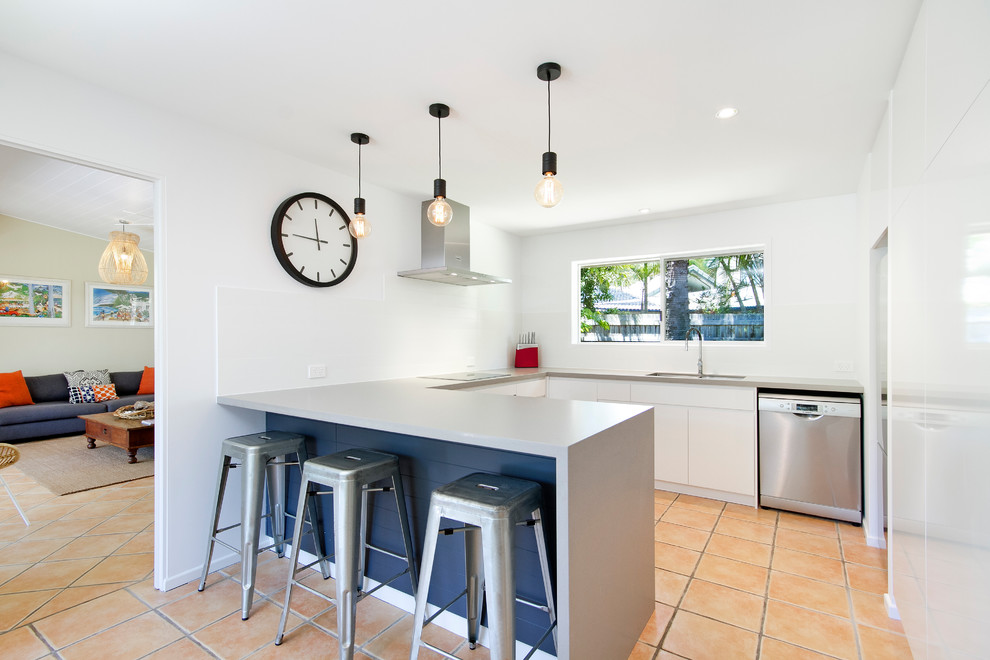 Inspiration for a mid-sized beach style u-shaped separate kitchen in Sunshine Coast with a double-bowl sink, white cabinets, white splashback, porcelain splashback, stainless steel appliances, terra-cotta floors and with island.