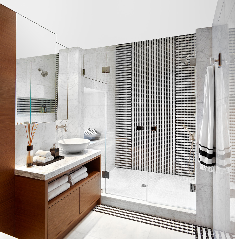 Inspiration for a mid-sized contemporary 3/4 bathroom in New York with flat-panel cabinets, medium wood cabinets, an alcove shower, black tile, black and white tile, white tile, mosaic tile, a vessel sink, multi-coloured floor, a hinged shower door, grey walls and marble benchtops.