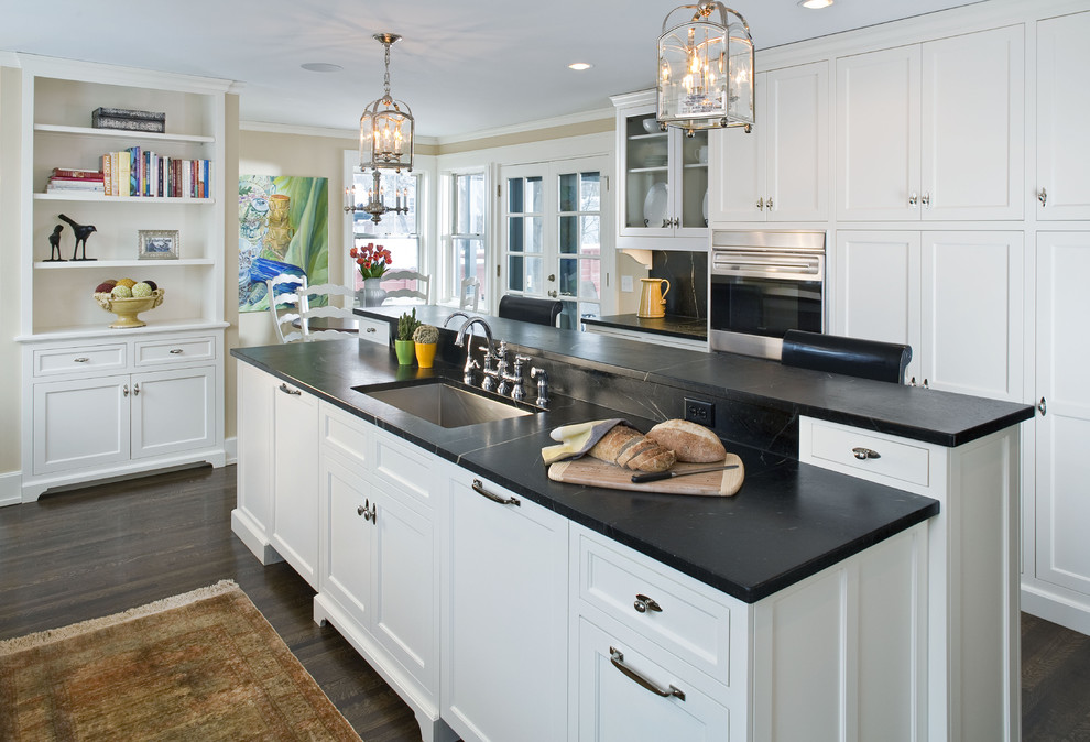 Design ideas for a large traditional l-shaped kitchen in Minneapolis with a single-bowl sink, recessed-panel cabinets, white cabinets, soapstone benchtops, black splashback, stone slab splashback, black appliances, dark hardwood floors and with island.