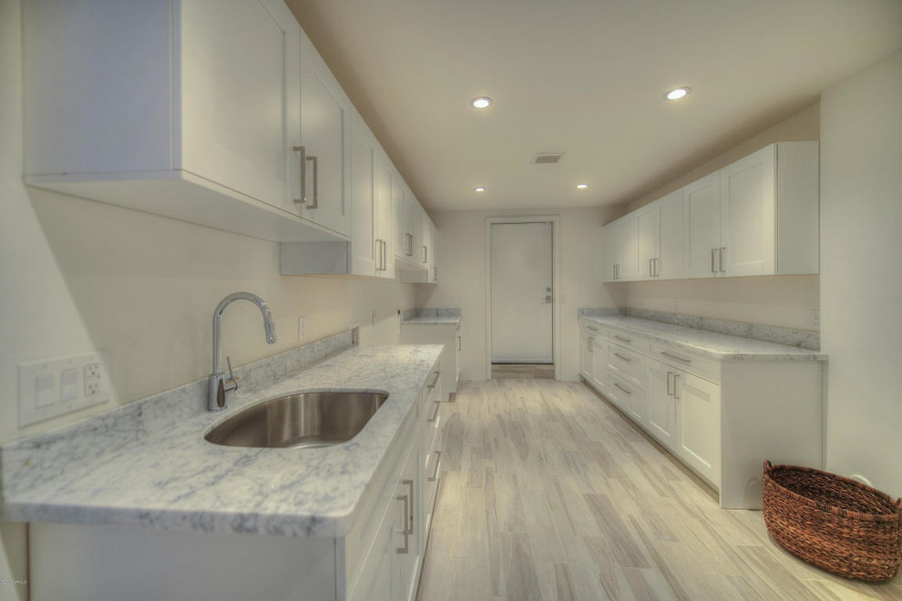 This is an example of a large transitional galley dedicated laundry room in Phoenix with an undermount sink, shaker cabinets, white cabinets, marble benchtops, white walls and a side-by-side washer and dryer.