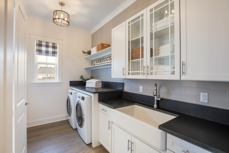 Design ideas for a mid-sized country single-wall dedicated laundry room in Jacksonville with a farmhouse sink, glass-front cabinets, white cabinets, granite benchtops, white walls, medium hardwood floors, a side-by-side washer and dryer, brown floor and black benchtop.