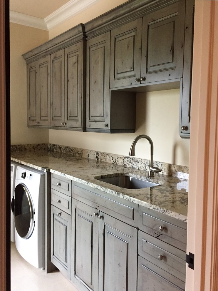 Design ideas for a mid-sized mediterranean single-wall dedicated laundry room in Miami with an undermount sink, raised-panel cabinets, granite benchtops, yellow walls, travertine floors, a side-by-side washer and dryer, beige floor, multi-coloured benchtop and grey cabinets.